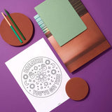 Flat lay of a printable mindfulness page, colored pencils, and notebooks on a vibrant purple background.