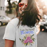 Woman wearing a t-shirt with 'I can buy myself flowers' text and floral design outdoors.