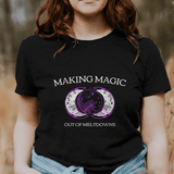 Person wearing a black t-shirt with 'Making Magic Out of Meltdowns' design in a field.