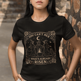 Woman wearing a black t-shirt with a graphic design and text, standing against a stone wall.