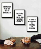 Motivational wall decor featuring three framed quotes about strength, healing, and self-worth on a table with drinks.