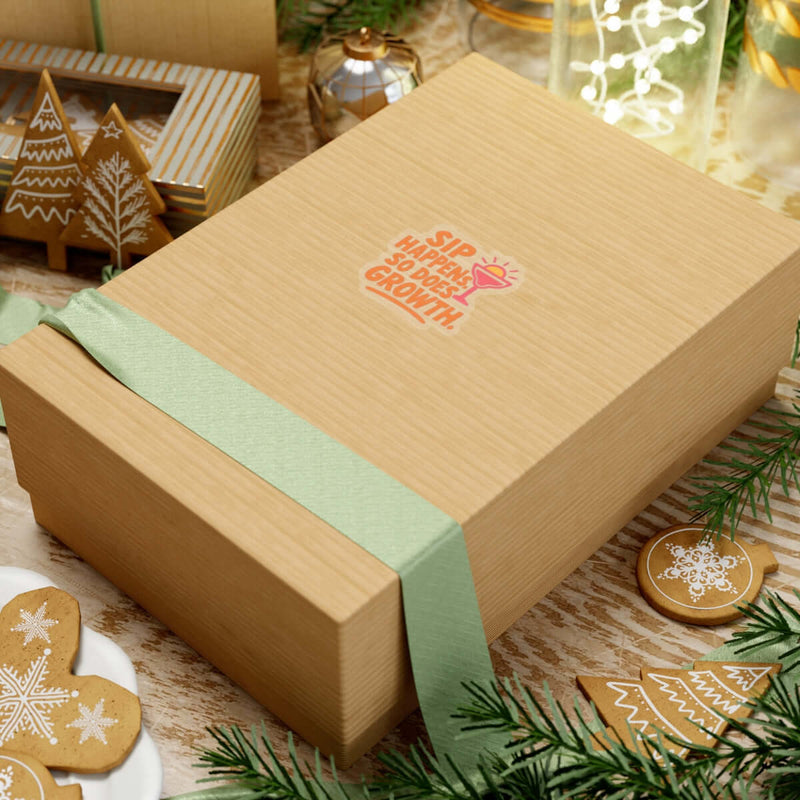 Wooden gift box with green ribbon, featuring 'Sip Happens' mantra, surrounded by festive decorations and baked treats.
