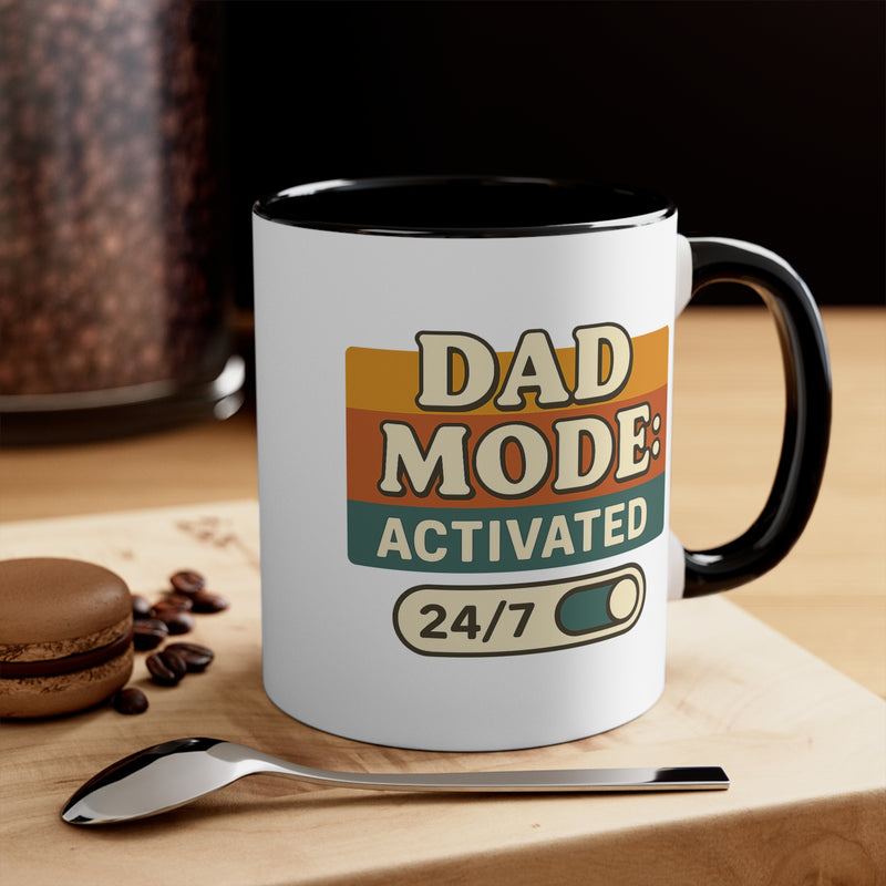 Mug with 'Dad Mode Activated 24/7' text on a wooden surface with coffee beans and a spoon.