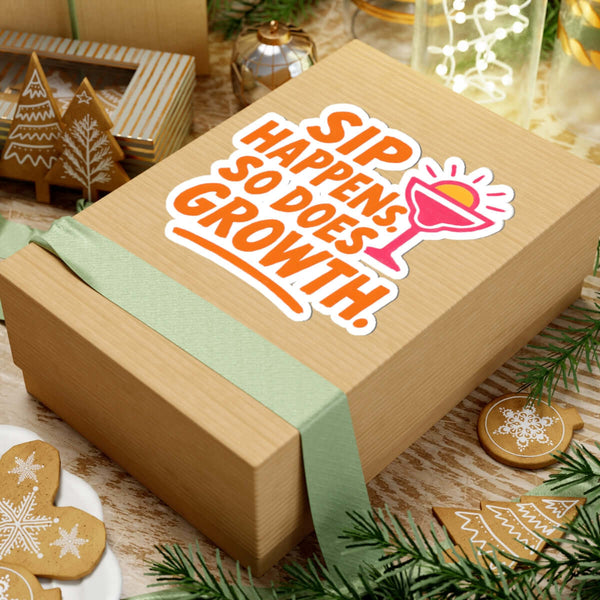 Colorful sticker on a gift box reading 'Sip Happens, So Does Growth' surrounded by festive decor.