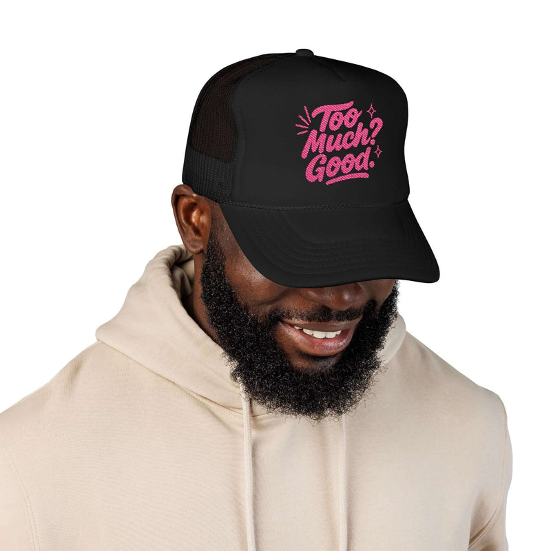 Man smiling while wearing a black foam trucker hat with pink "Too Much Good" embroidery.