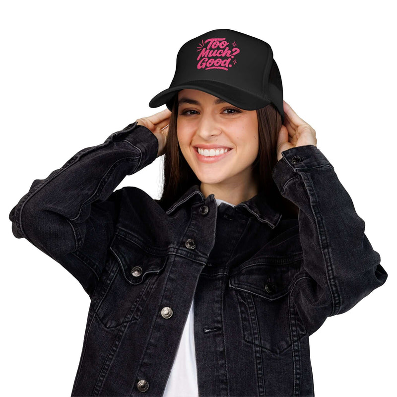 Young woman wearing a black foam trucker hat with the text 'Too Much Good.' styled casually in a denim jacket.