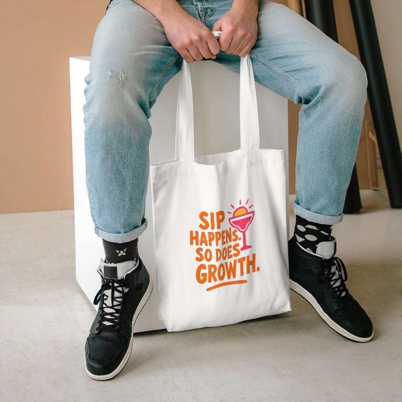 Sip Happens Growth Tote Bag on a person sitting, showcasing a fun eco-friendly design for beach and grocery use.