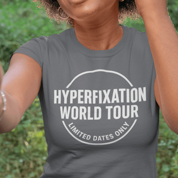 Person wearing a gray t-shirt with 'Hyperfixation World Tour' text outdoors.