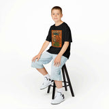 Boy sitting on stool wearing Global Halloween Kids Tee featuring 'Creep It Real & Be Kind' design.
