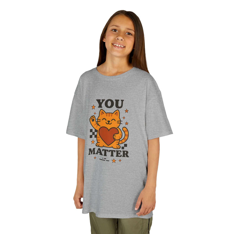 Smiling child wearing a gray tee with cartoon cat and 'YOU MATTER' text, promoting positivity and self-love.