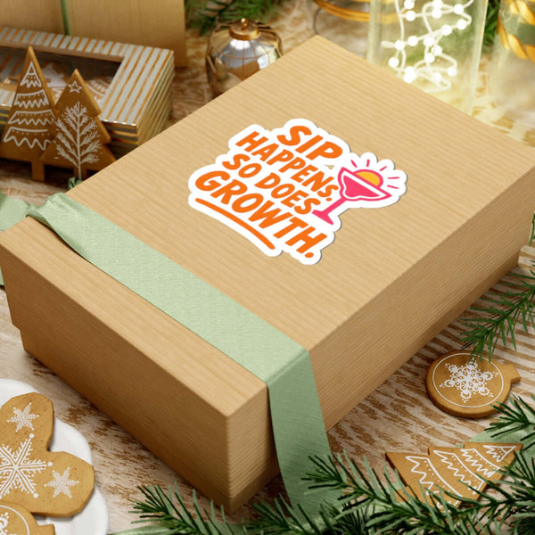 Colorful sticker on a gift box saying 'Sip Happens, So Does Growth' surrounded by festive decorations.