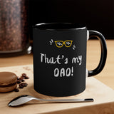 Black mug with 'That's my DAD!' text on a wooden surface with coffee beans and a spoon.