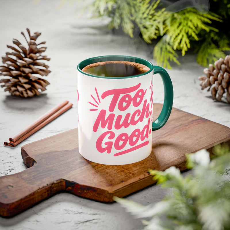 Colorful affirmation coffee mug with the phrase 'Too Much Good!' on a wooden cutting board, surrounded by pinecones.