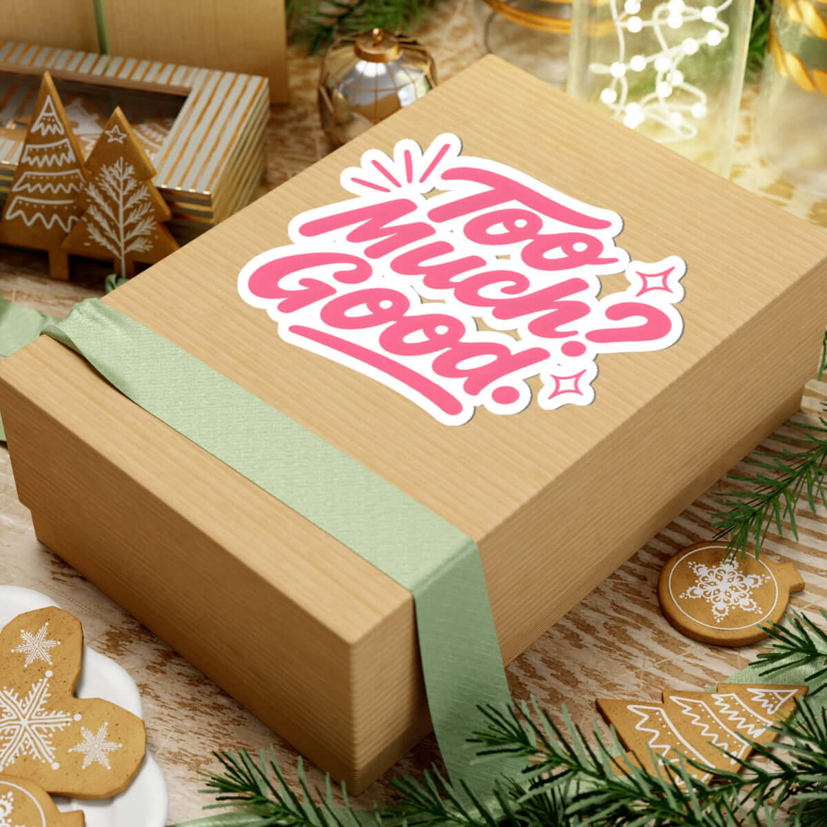 Gift box with a decorative 'Too Much? Good!' kiss-cut sticker, surrounded by holiday decor.