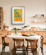 Inspirational wall art print saying 'Sip Happens. So Does Growth' in a bright kitchen setting.