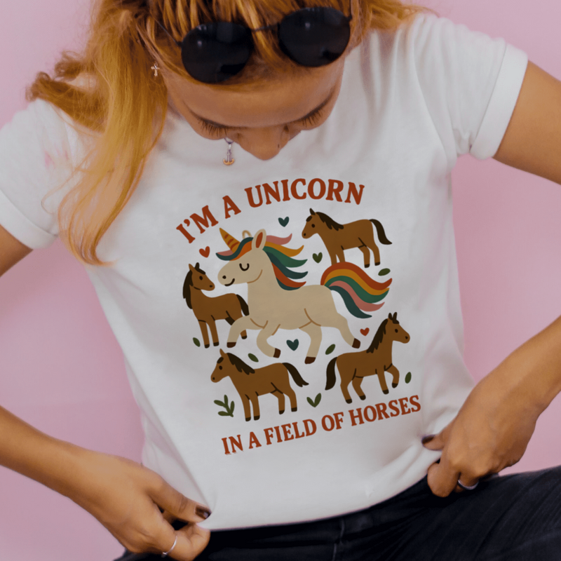 Person wearing a white t-shirt with a unicorn graphic and text on a pink background