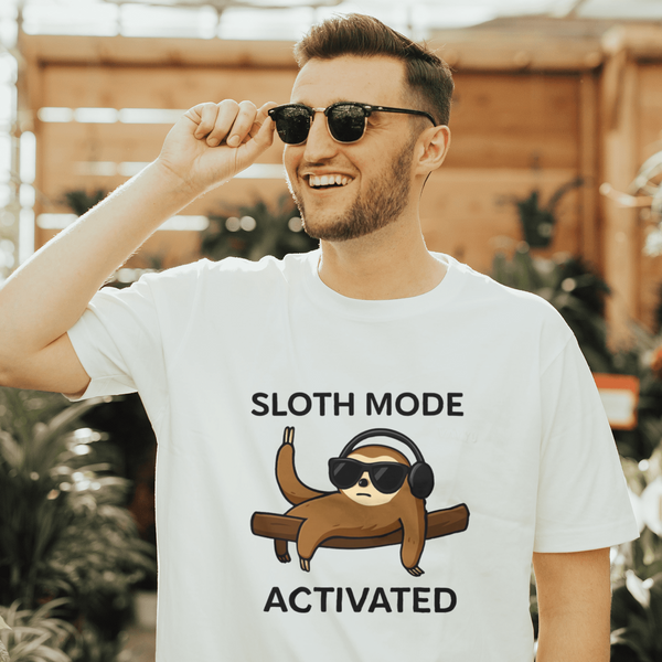 Man wearing a t-shirt with a sloth graphic and text in a greenhouse setting