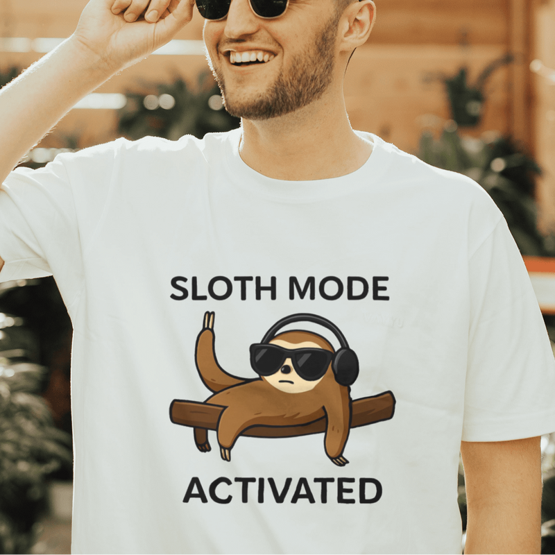Man wearing a t-shirt with a sloth graphic and text in a greenhouse setting