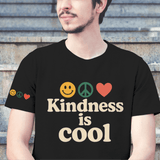 Person wearing a black t-shirt with 'Kindness is Cool' text and emojis, sitting on steps.