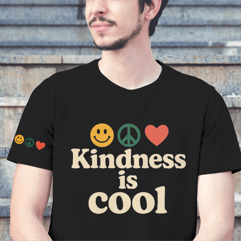 Person wearing a black t-shirt with 'Kindness is Cool' text and emojis, sitting on steps.