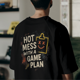 Person wearing a black t-shirt with text and graphics, standing in a room with shelves and a couch.
