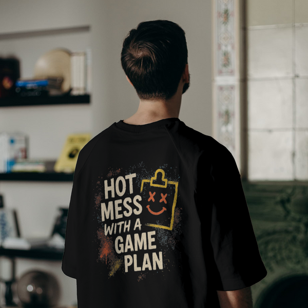 Person wearing a black t-shirt with text and graphics, standing in a room with shelves and a couch.