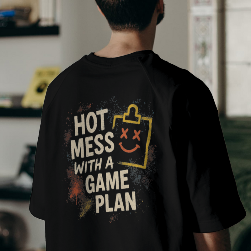 Person wearing a black t-shirt with text and graphics, standing in a room with shelves and a couch.