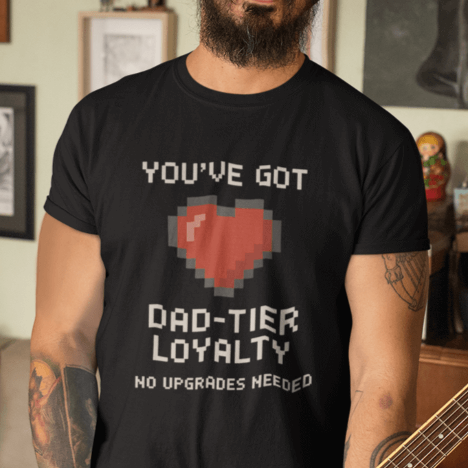 Man wearing a black t-shirt with a humorous graphic and text, standing in a room with decor.