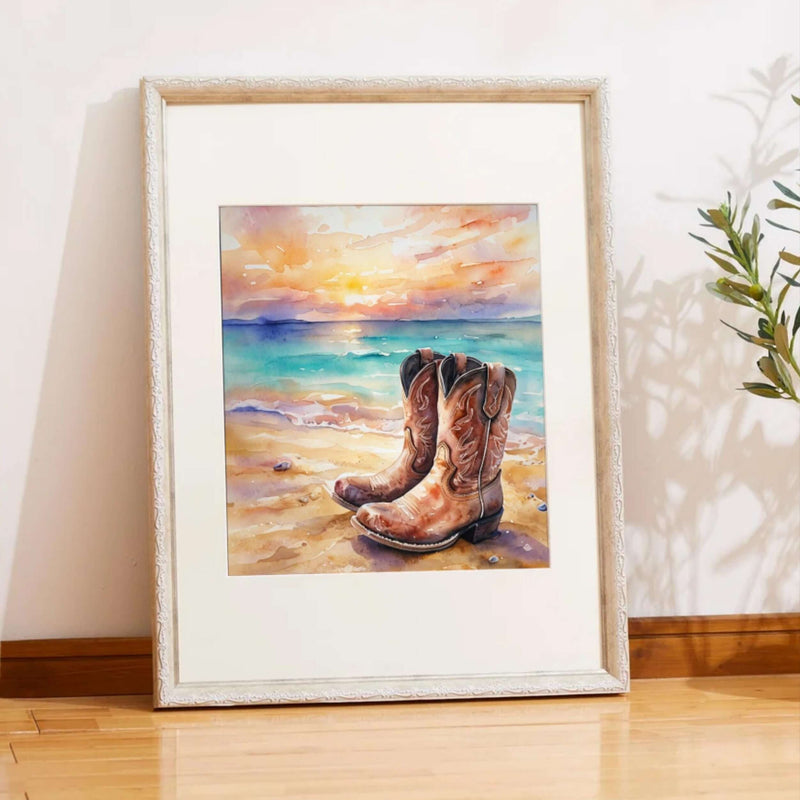 Framed artwork of cowboy boots on a beach with a sunset.
